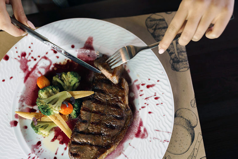 Female hands cutting road kill steak on plate with vegetables and red wine a jus splatter