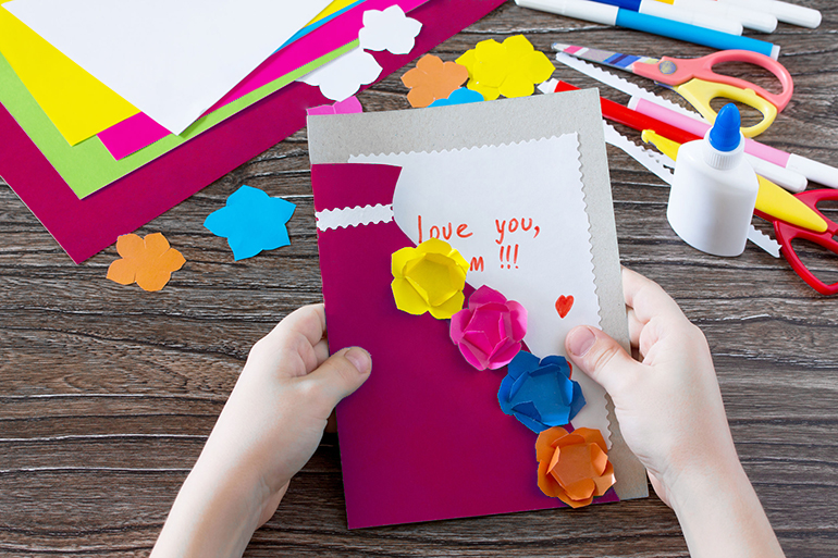 A child is holding a greeting card with flowers on Mother's Day. Children's art project, craft for children. Handmade. Craft for children. Valentine's Day