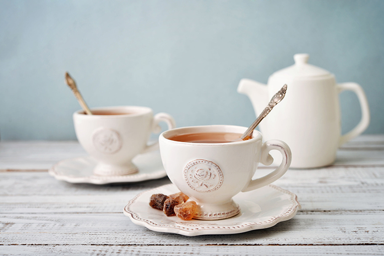 Cup of tea and sugar with teapot over blue background