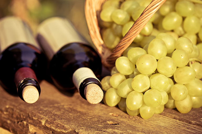 red and white wine bottles and bunch of grapes in basket on wooden table. retro toned image