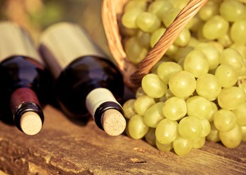 red and white wine bottles and bunch of grapes in basket on wooden table. retro toned image