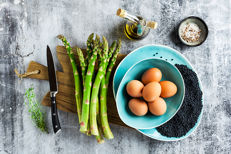 ingredients for cooking asparagus, black lentils, olive oil and eggs on the table on grey stone table