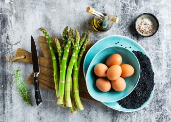 ingredients for cooking asparagus, black lentils, olive oil and eggs on the table on grey stone table