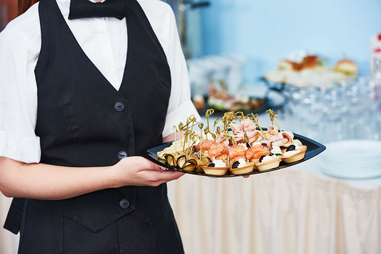 waitress catering service. female staff servicing dish full of snack food at restaurant event