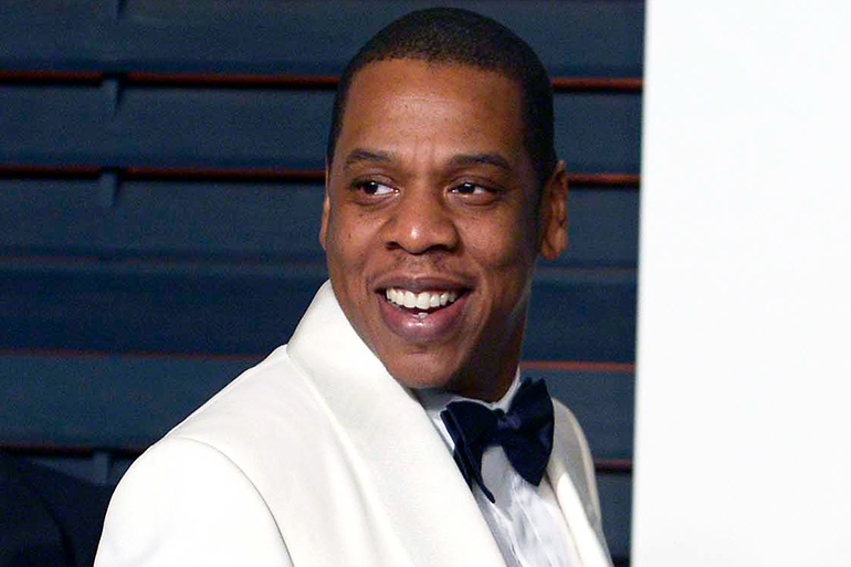 Jay-Z smiling while wearing a white tuxedo with black tie in 2015