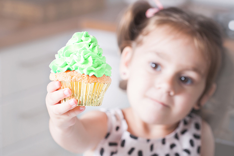 Cute little girl holding birthday cupcakes in kitchen. Festive and holiday concept