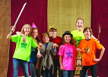 Young actors holding costume pieces smile and pose for the camera
