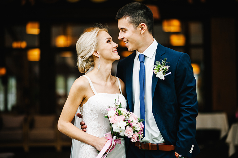 Romantic couple newlyweds, bride and groom holding bouquet of pink and purple flowers and greens with ribbon at the wedding ceremony. Happy and joyful wedding moment.