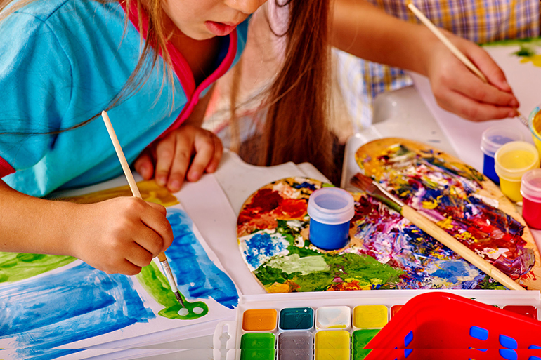 Close up of girl with brush painting in kindergarten .