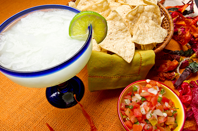 Margarita, chips and salsa on an orange backgroud with chili peppers.