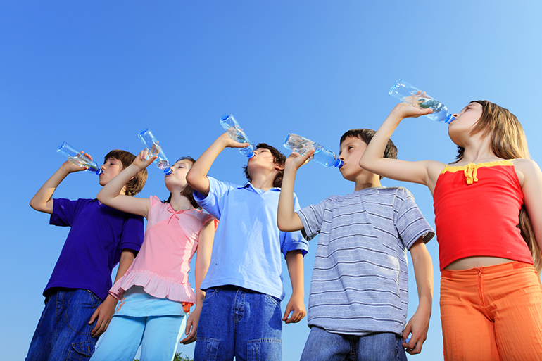 Children drinking water from bottles against the blue sky.
