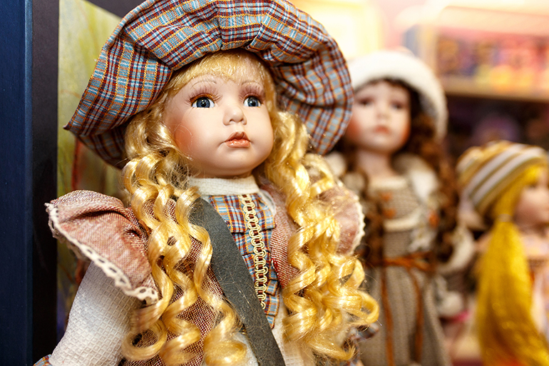 Close-up of beautiful porcelain doll with blond hair and blue eyes, sky blue vintage dress. Little princess games.