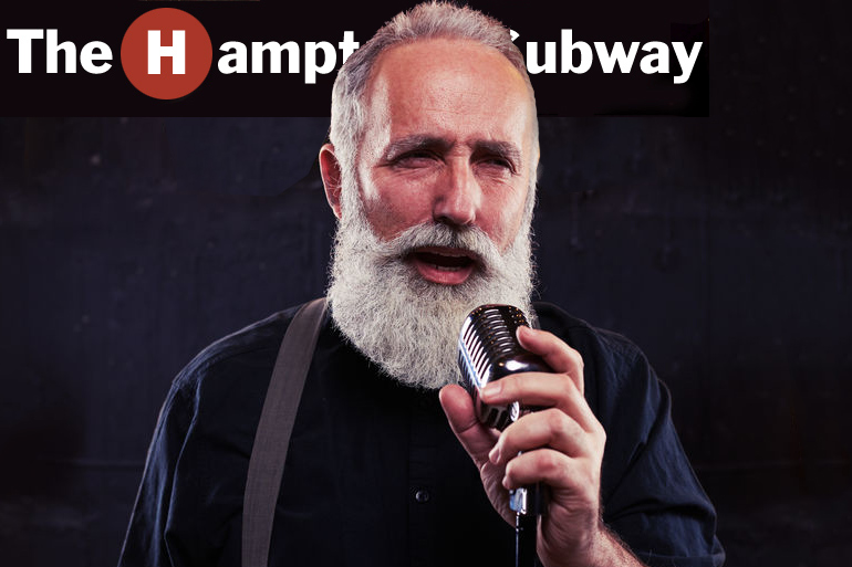 Hamptons Subway announcer Harold Gooding on microphone in front of Hamptons Subway sign