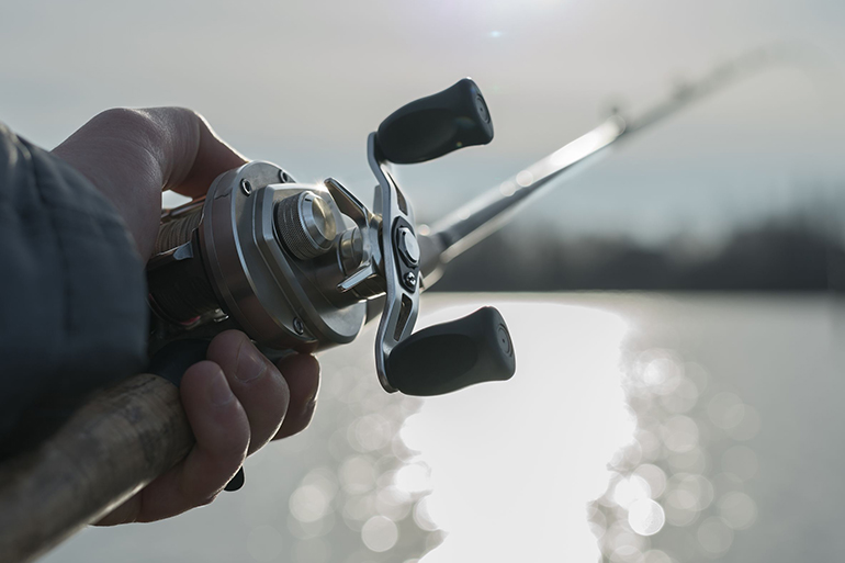 Angler on the river with close up baitcasting reel in hilights