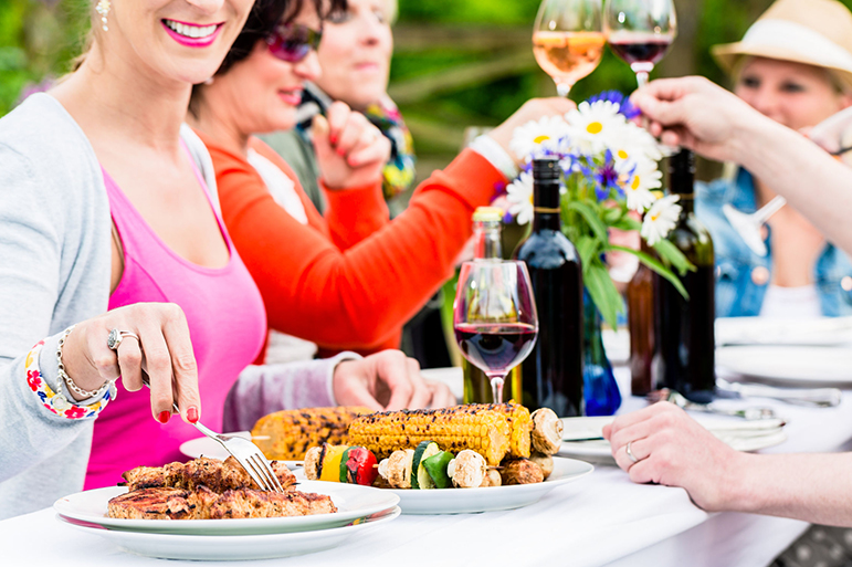 Women and men celebrating garden party, eating and drinking together