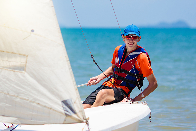 Young man sailing. Teenager boy on sea yacht. Healthy water sport. Yachting class for teen age sailor. Ocean vacation on boat. Regatta on tropical island. Beach and sail activity.