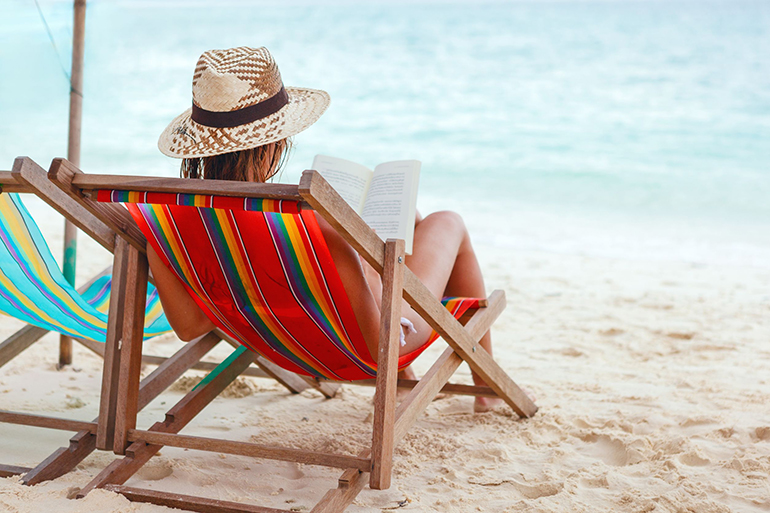 young beautiful woman sitting on beach reading a book