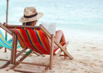 young beautiful woman sitting on beach reading a book