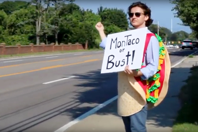 Guy in taco suit hitchhiking with "MonTaco or Bust" sign