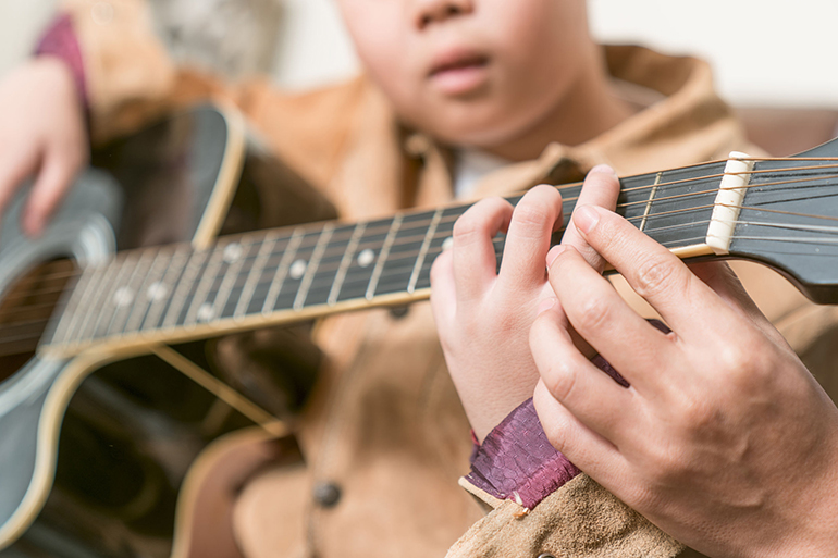 teacher giving guitar lessons to pupil in a classroom