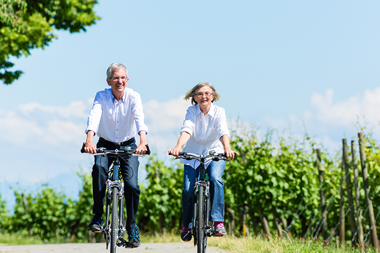 Senior woman and man using bike in summer in vineyard