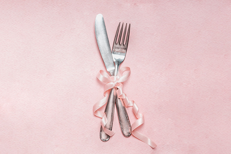 Romantic dinner table place setting with ribbon decoration on pink pale background, top view, close up