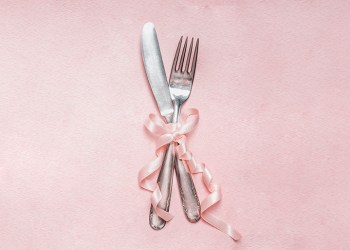 Romantic dinner table place setting with ribbon decoration on pink pale background, top view, close up