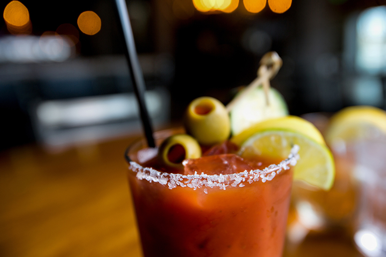 Cold bloody mary cocktail garnished with lemon, lime, green olive and salt