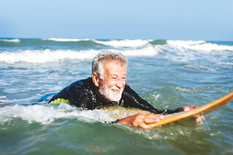 elderly surfer with beard paddling in the ocean