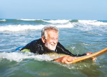 elderly surfer with beard paddling in the ocean
