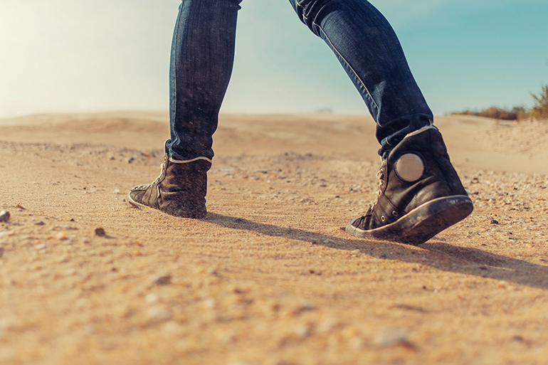 Unrecognizable woman walking on sand, view of legs.