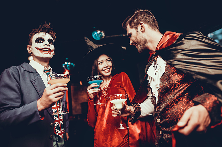 Young People Drinking Cocktails at Halloween Party. Group of Young Smiling Friends Wearing Halloween Costumes Drinking Cocktails and having Fun in Nightclub. Celebration of Halloween