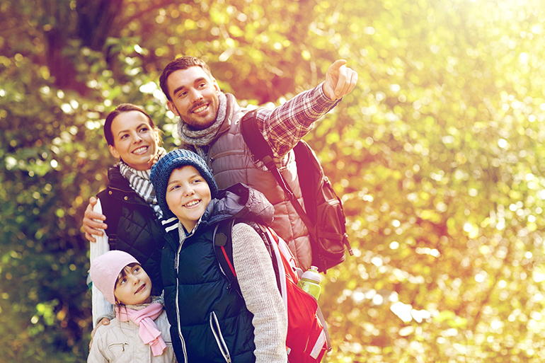 hike, travel, tourism and people concept - happy family walking with backpacks in woods