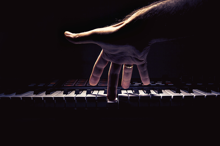 Playing a keyboard, one male hand playing, accentuated contrasts.