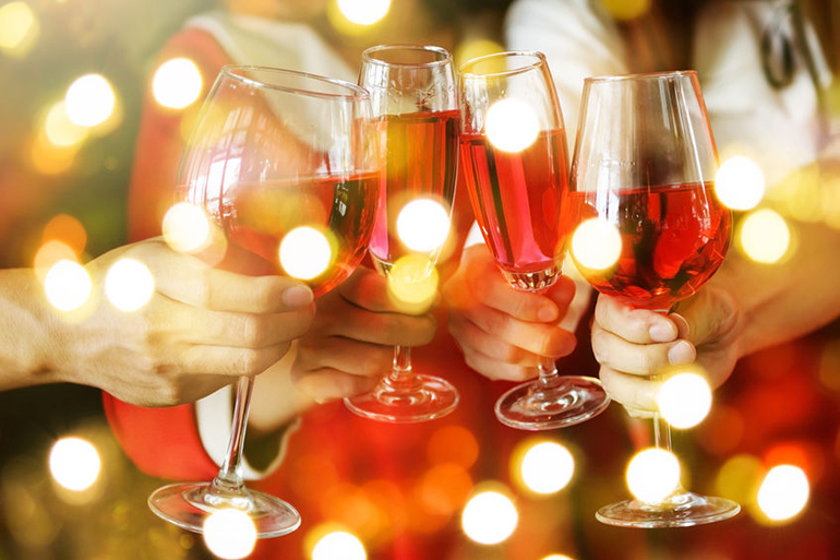 Hands holding wine glasses toasting the holidays with Christmas lights flickering
