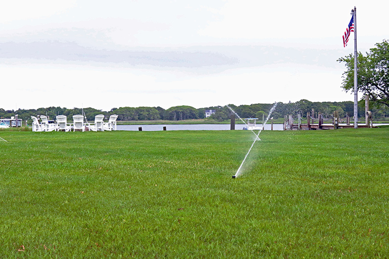 Sprinklers watering lawn near bay and flagpole Peconic