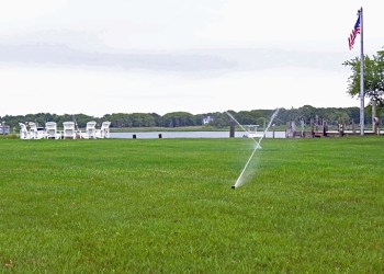 Sprinklers watering lawn near bay and flagpole Peconic