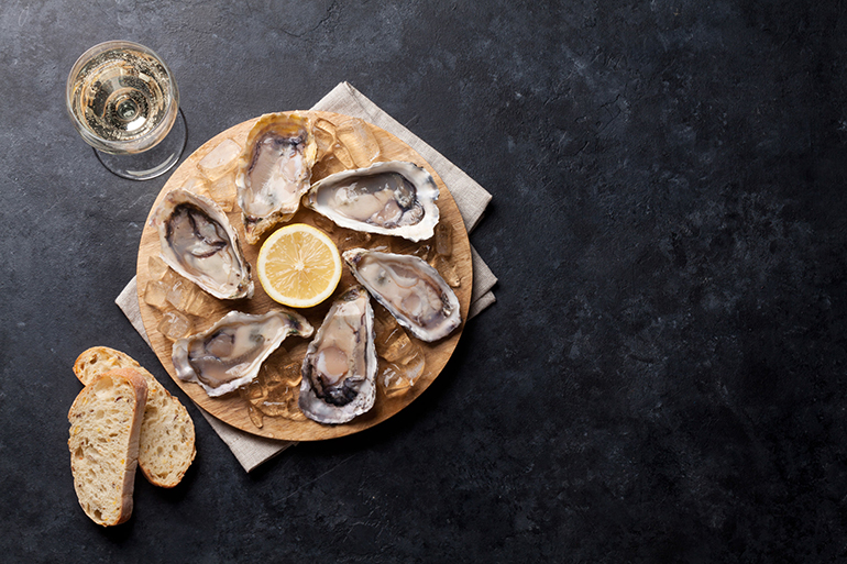 Opened oysters, ice and lemon on board and white wine on stone table. Top view with copy space