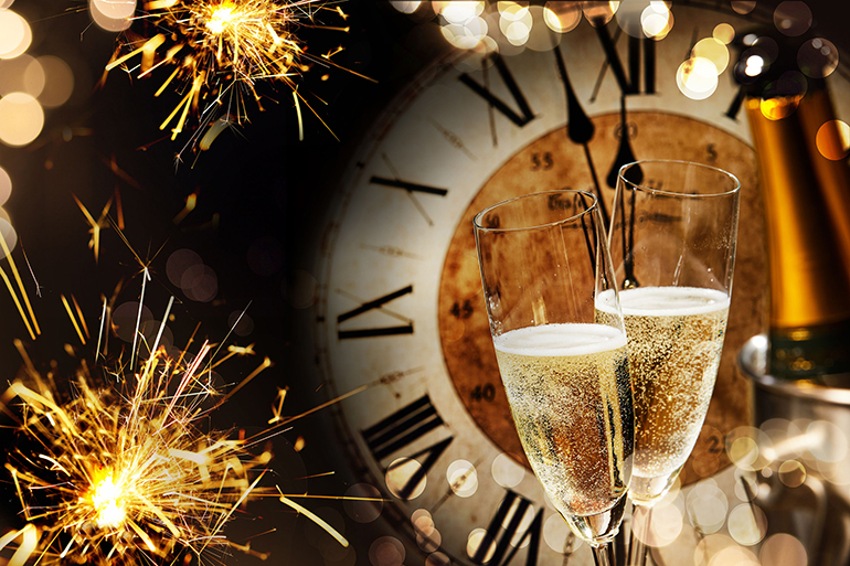 Festive New Years background with sparklers and champagne in front of a clock counting down to midnight with sparkling bokeh on darkness