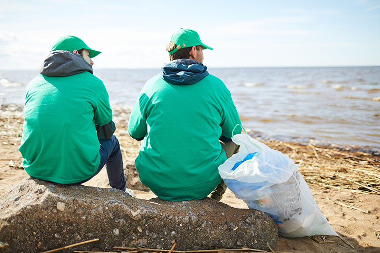 Back view of two workers of ecological organization sitting on big stone in front of waterside