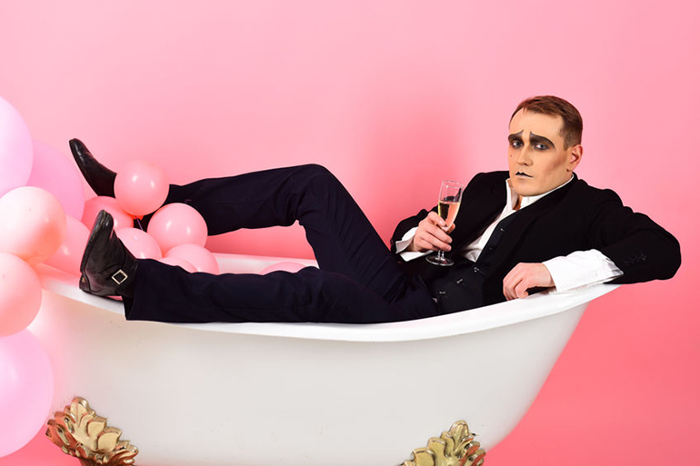 McSqueaks comedian wearing suit and drinking champagne in bathtub with pink balloons