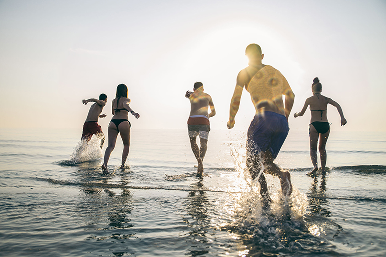 Group of happy friends running in to water at sunset - Silhouettes of active people having fun on the beach on vacation - Tourists going to swim on a tropical island