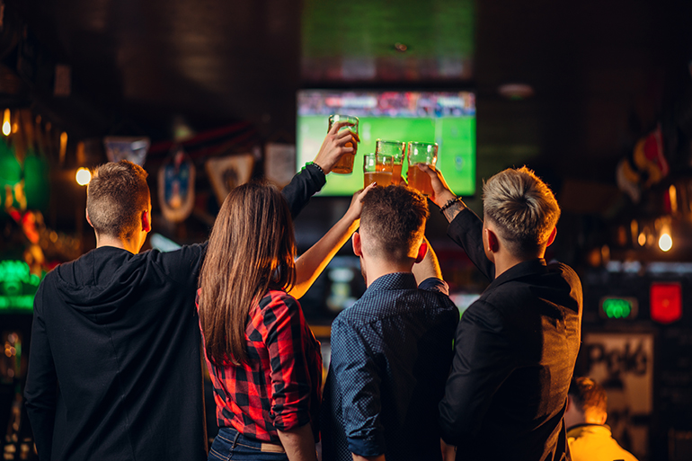 Fun friends watches football on TV and raised their glasses with beer in a sport bar, happy fans, celebration of the victory in game