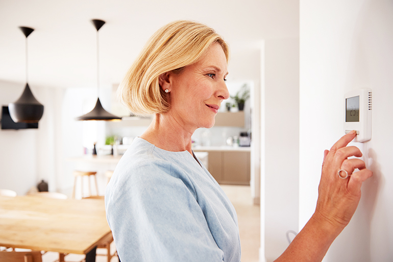 Close Up Of Mature Woman Adjusting Central Heating Temperature At Home On Thermostat