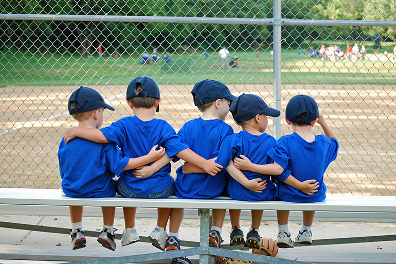 five little boys put their arms around each other before their baseball game