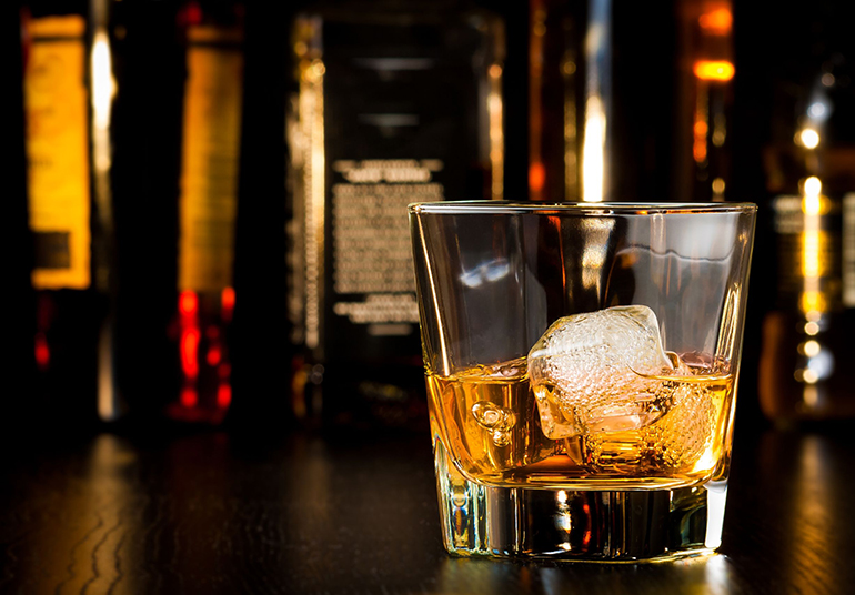 whiskey glass with ice in front of bottles