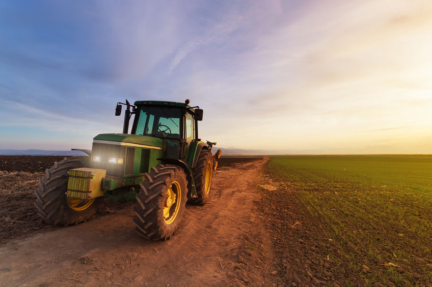 Tractor on farm field at sunset after plowing