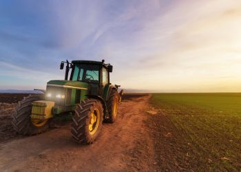 Tractor on farm field at sunset after plowing