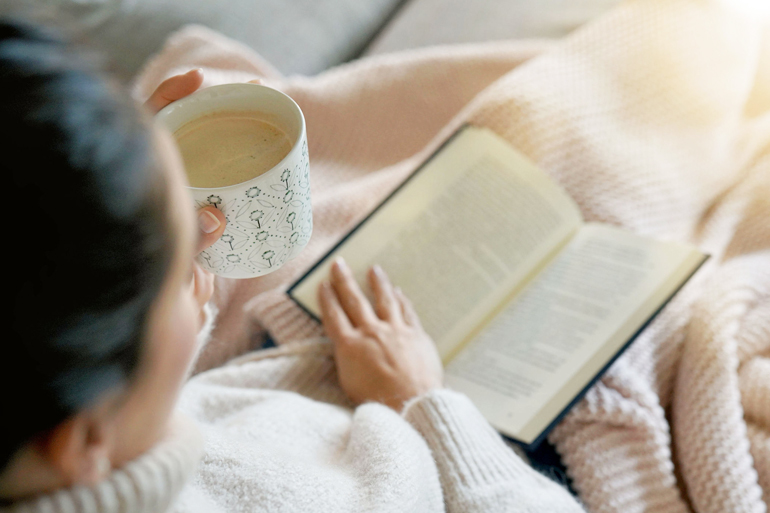 Cosy brunette at home on couch with hot drink and reading