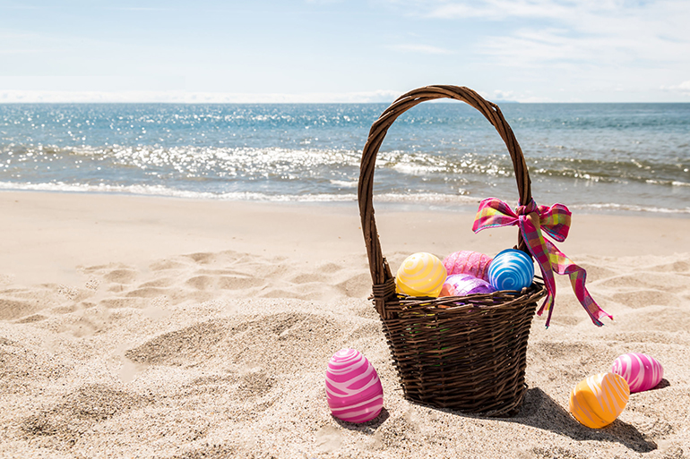 Easter basket with color eggs on the sandy beach near ocean